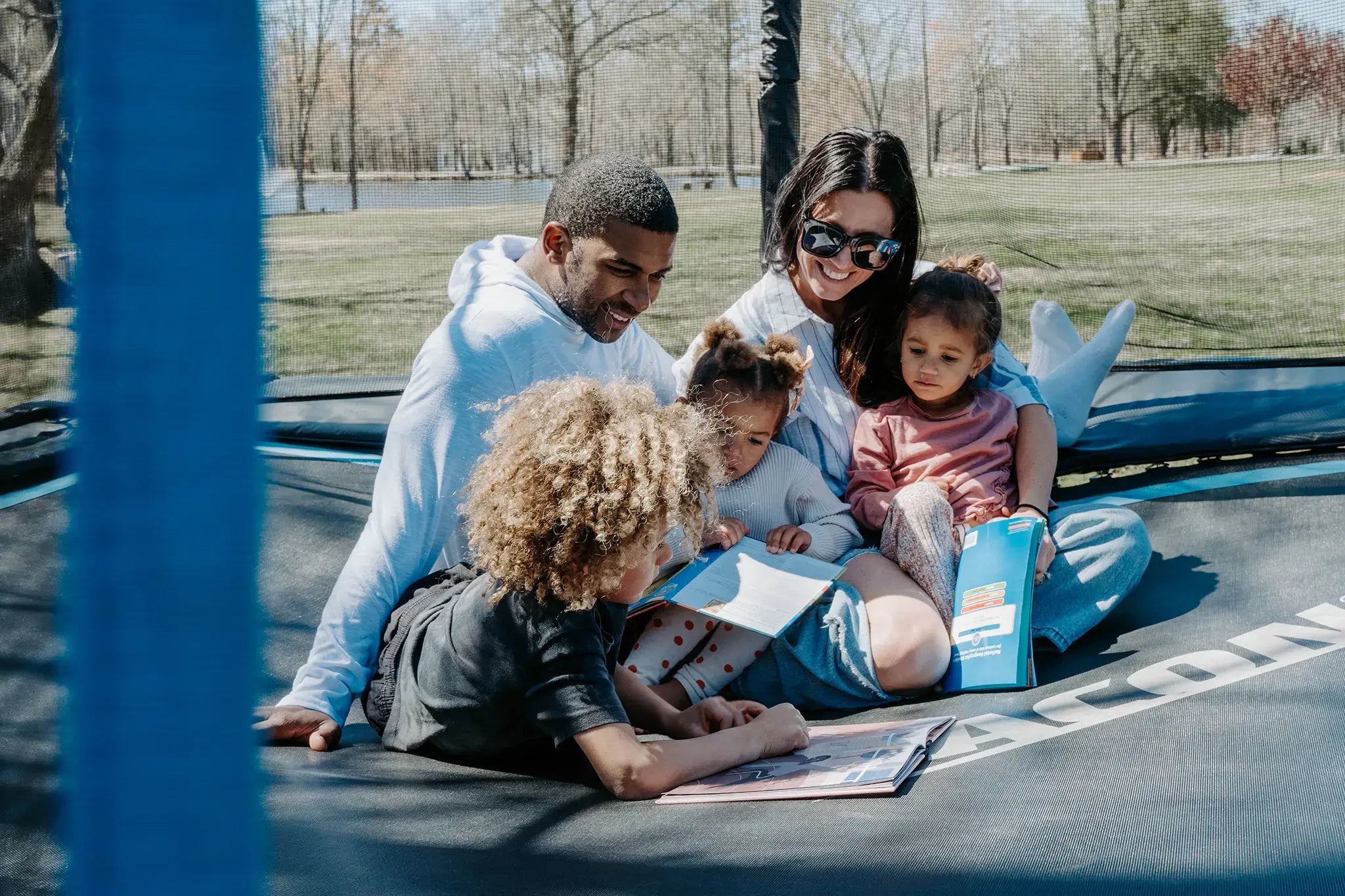 Family sitting on a Acon trampoline, reading together outdoors.