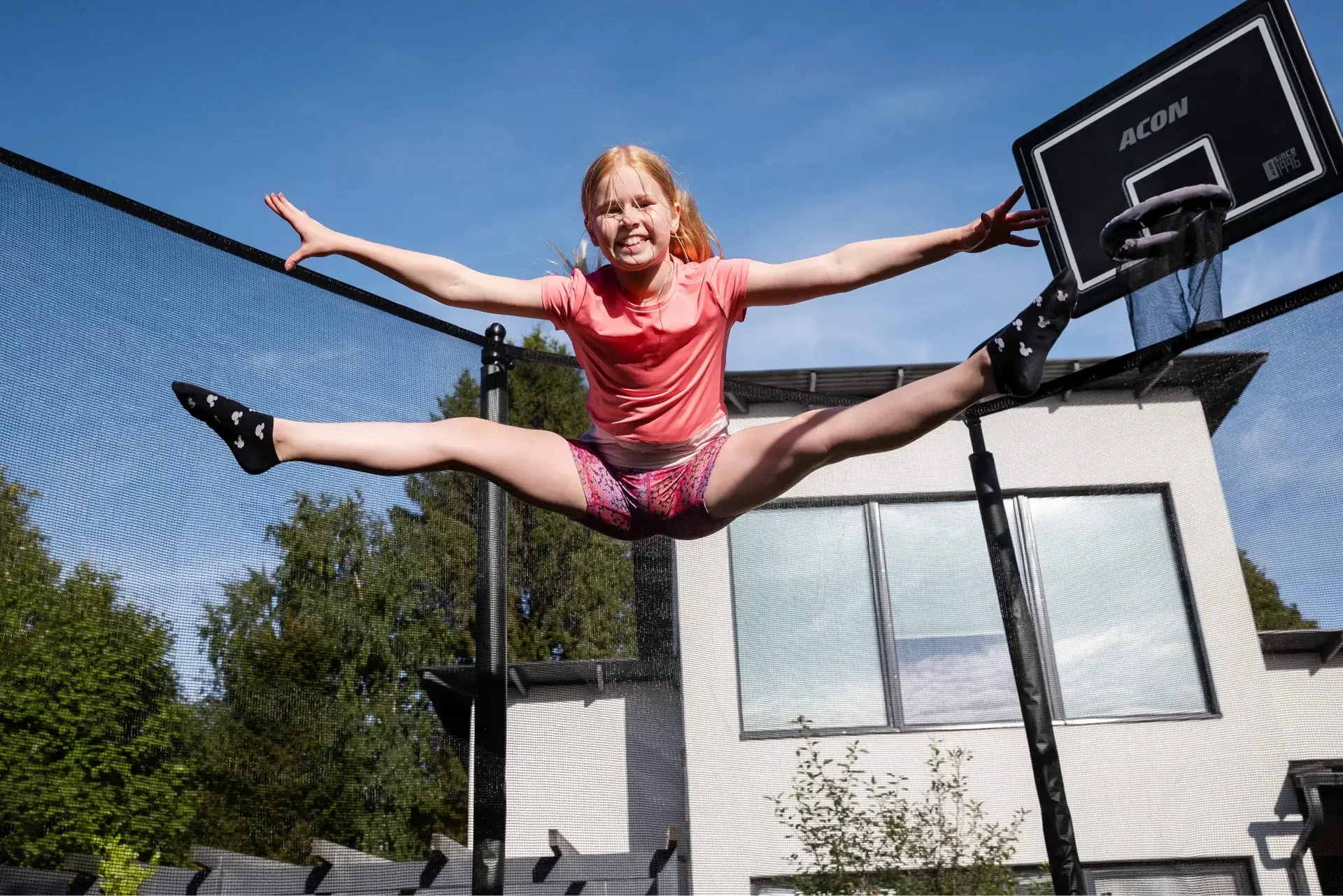 Girl jumping high on a trampoline in front of a house, performing a split.