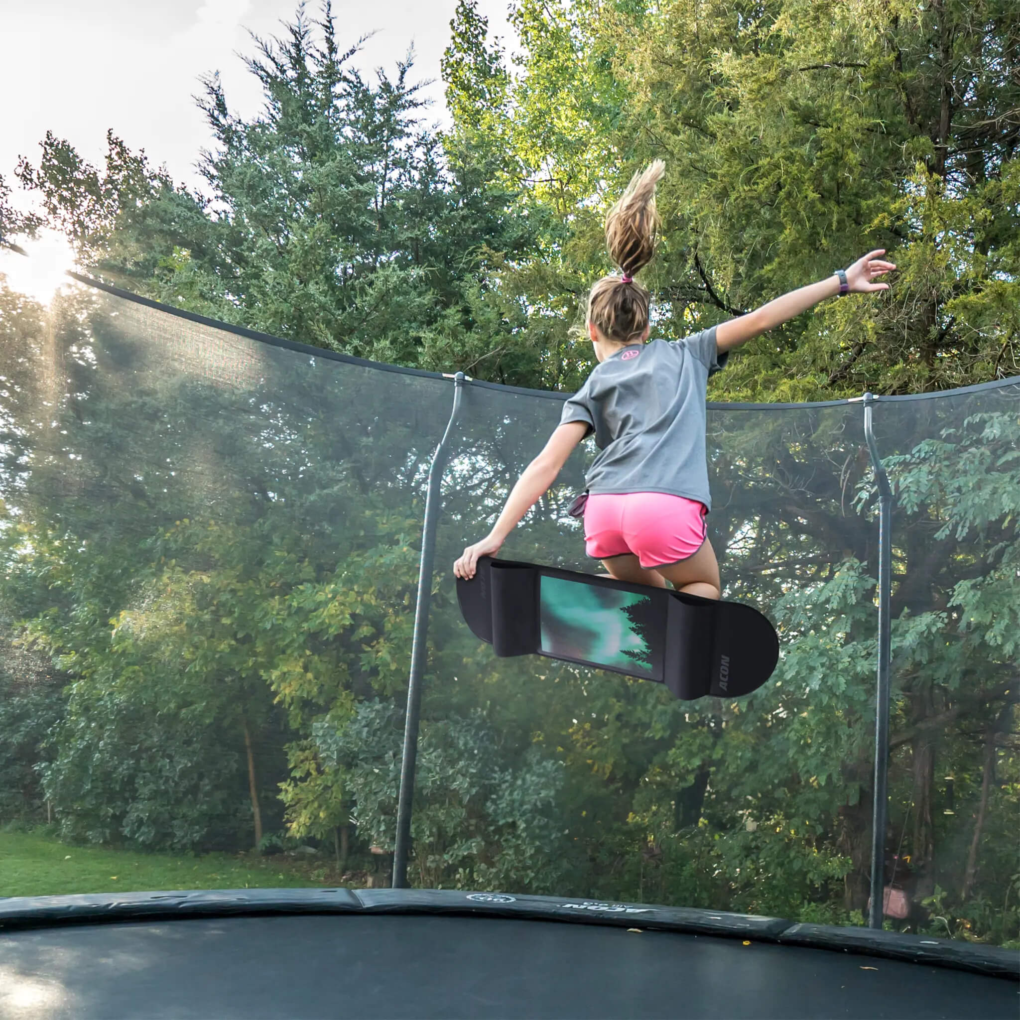 A girl is jumping on a trampoline with an Acon Trampoline Skateboard.