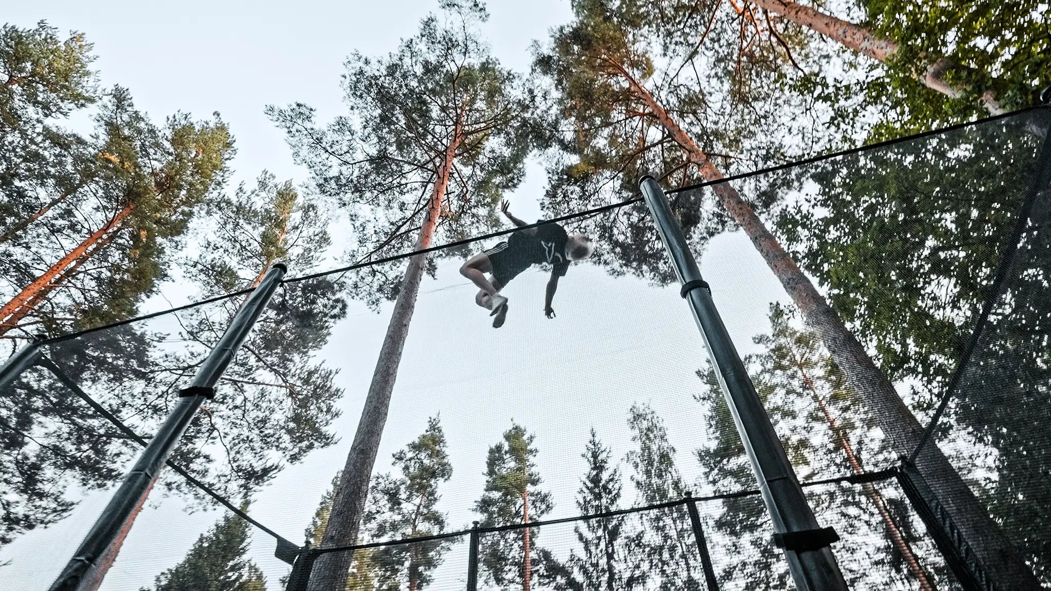 Man jumping high on a trampoline with safety net.