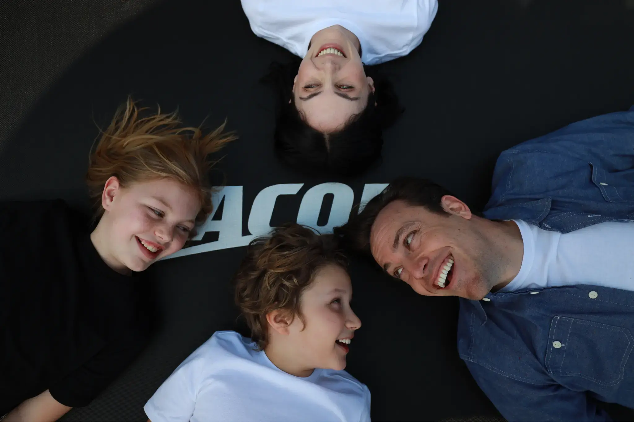 Happy family laying on a Acon trampoline looking at each others and smiling. 