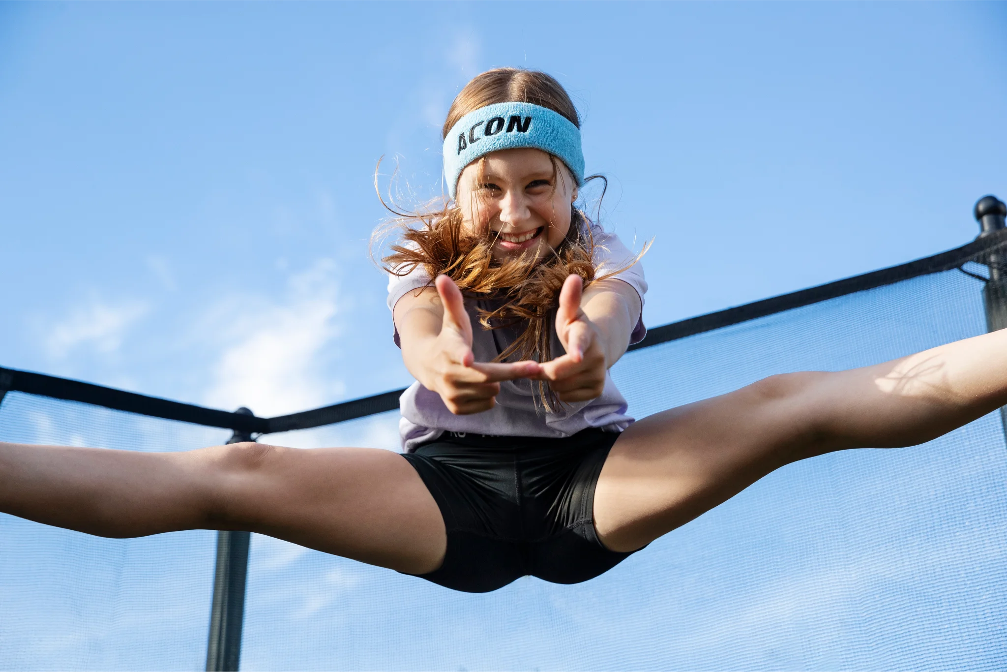 Smiling girl with an Acon headband jumping high doing a split.