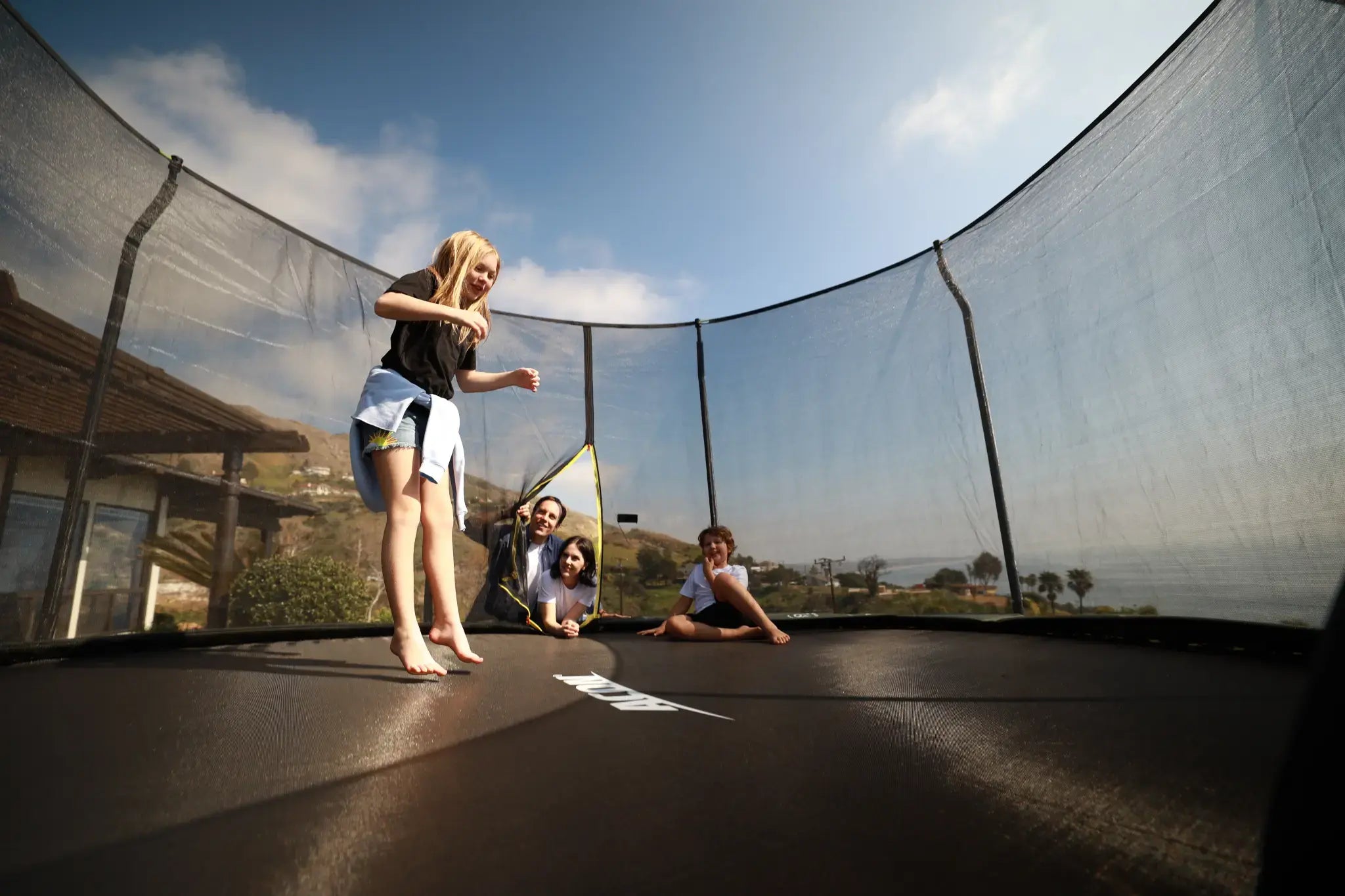 Child jumping on a round Acon trampoline with her family watching.