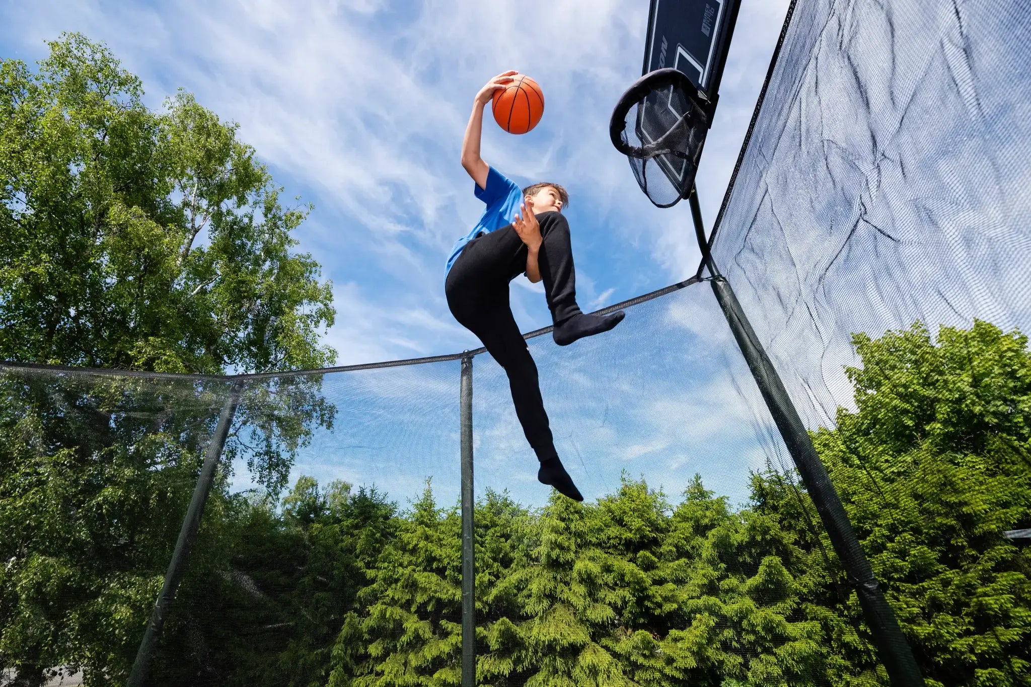 A child scoring with a basketball while jumping on trampoline.